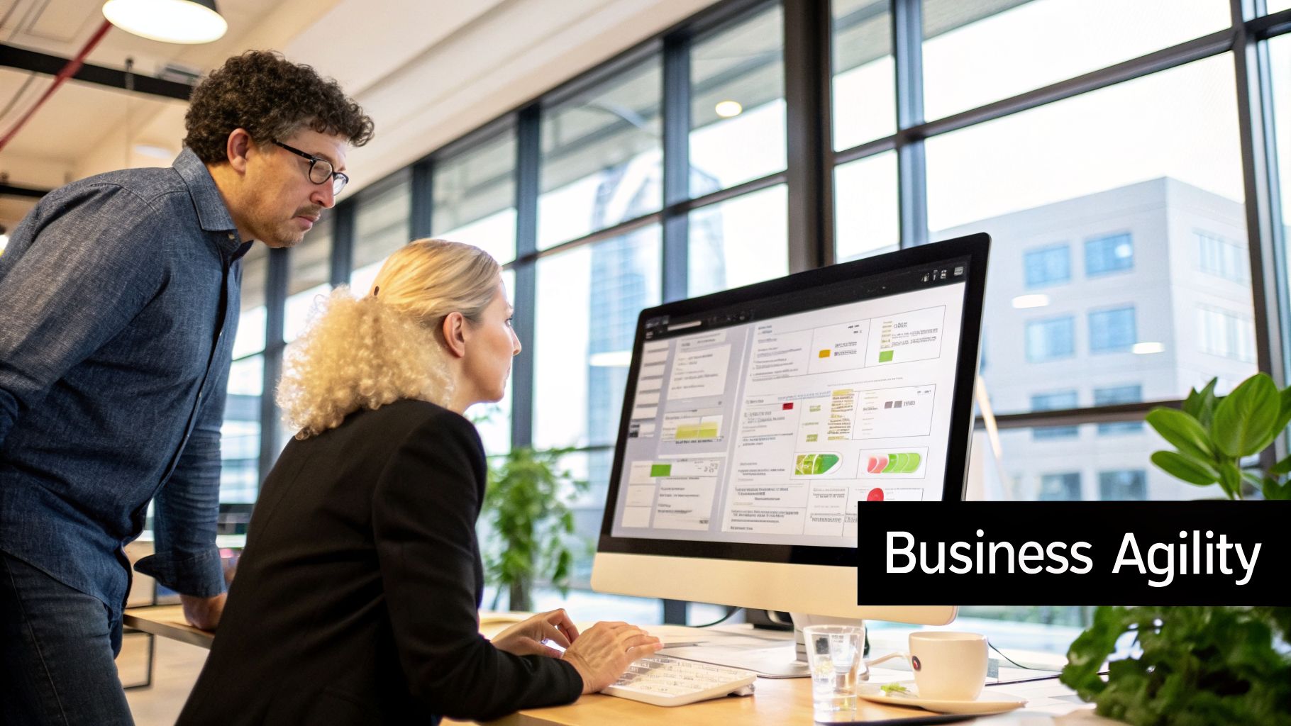Two business professionals analyze data on a computer screen, highlighting business agility strategies.
